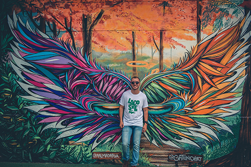 Uomo posa davanti a murales con ali